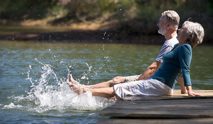 Pareja de jubilados relajándose en un muelle y salpicando agua, disfrutando de la vida con seguridad gracias a una asociación de confianza con BOK.