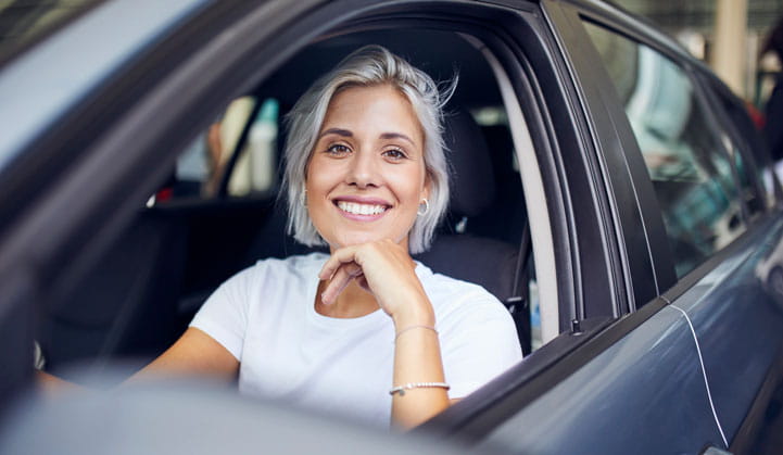 Persona sonriendo con la ventana baja del auto emocionada por encontrar buenas tasas de interés de préstamos con BOK Financial.